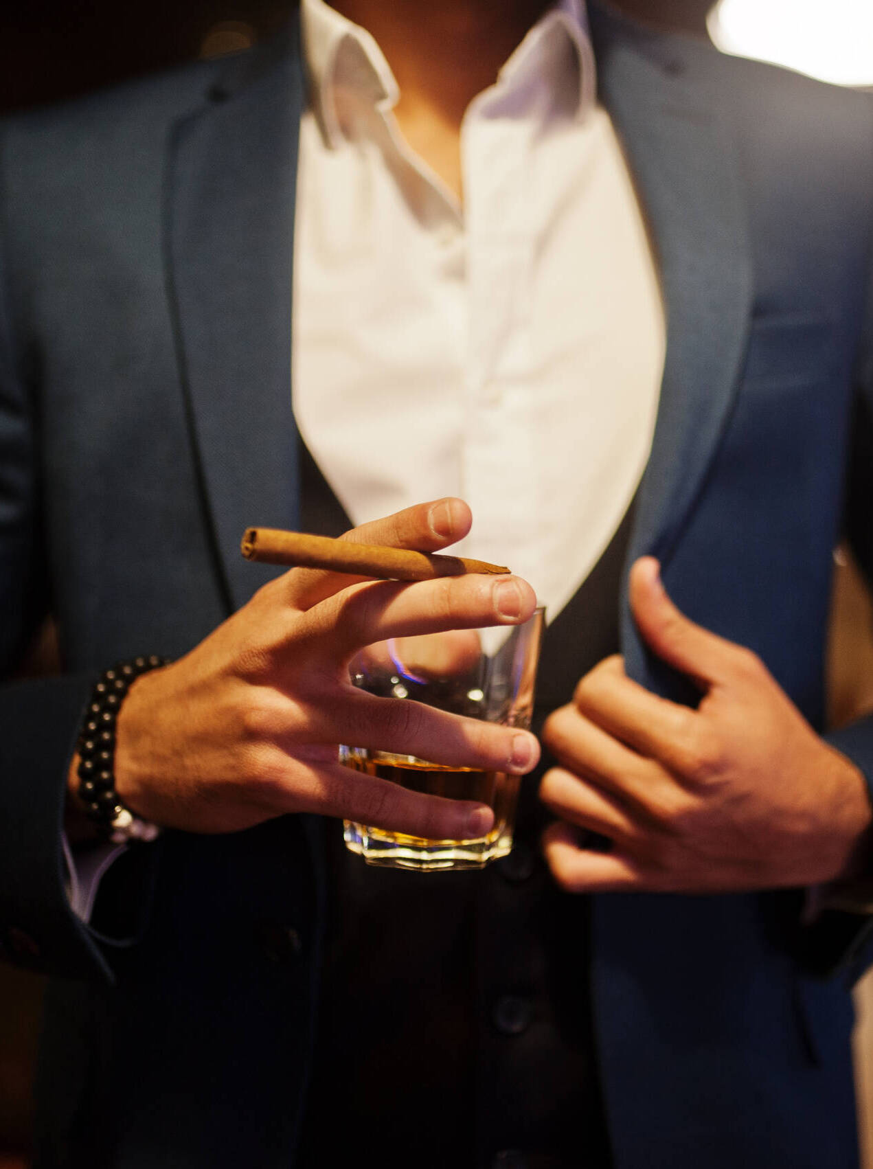 Close up hand of handsome well-dressed arabian man with glass of whiskey and cigar posed at pub.