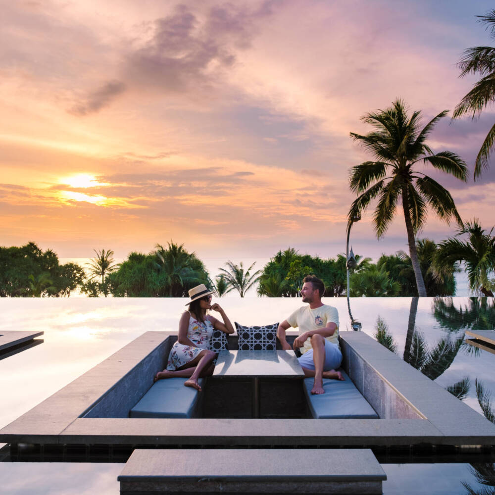 couple watching the sunset in an infinity pool on a luxury vacation in Thailand, man and woman watching the sunset on the edge of a pool in Thailand on vacation